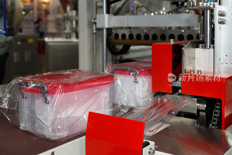 在塑料容器制造中，塑料收纳箱是用透明塑料薄膜包裹在包装机传送带上的。