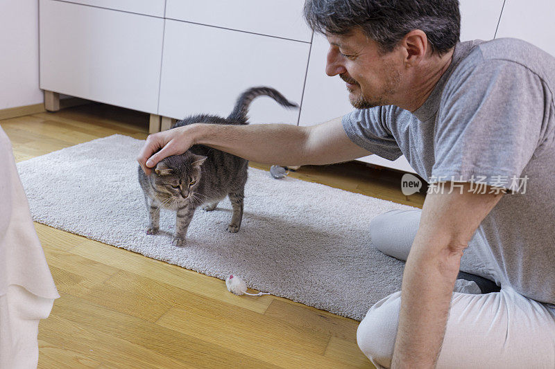 一个男人坐在地板上抚摸他的猫