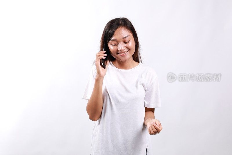 友好可爱的亚洲女孩抬头梦幻轻松，微笑愉快地将智能手机放在耳边，通过电话与朋友随意交谈，满足良好的移动连接，站在白色背景