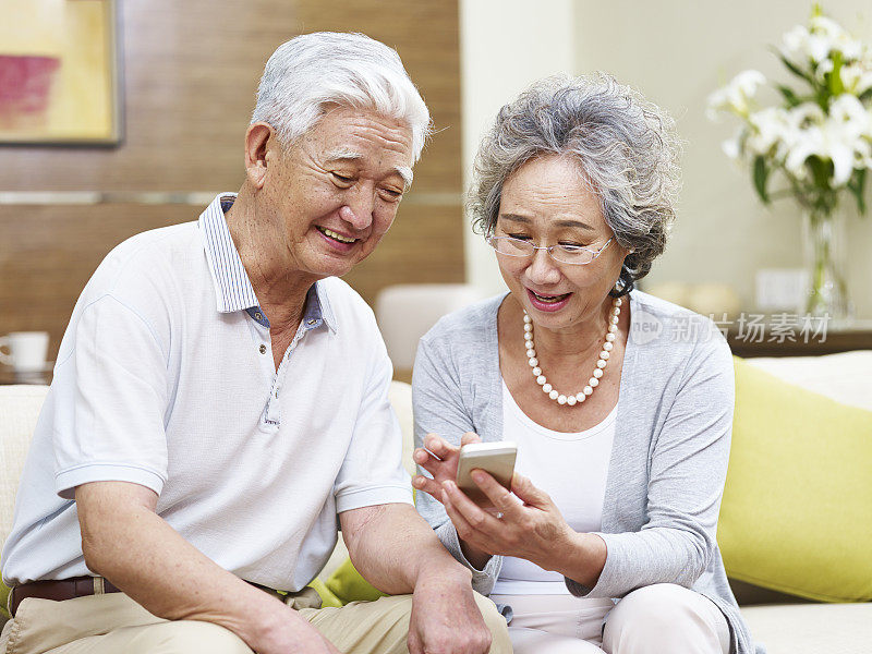 一对在家里使用手机的亚洲老年夫妇