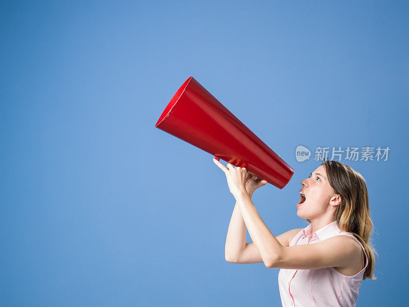 年轻美丽的女人大喊通过扩音器在天蓝色的背景