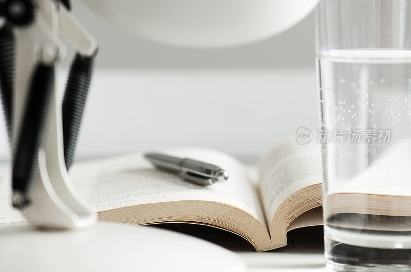 钢笔和打开的书在台灯和水后面的书桌上