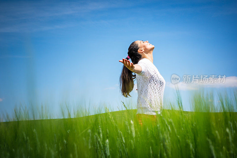 美丽的黑发女孩享受户外的绿色麦田。享受大自然。