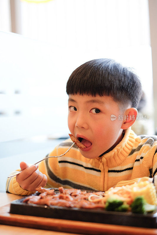 亚洲男孩在餐厅吃牛排