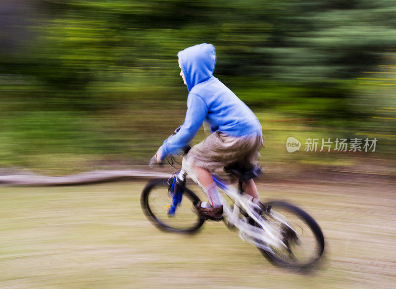 穿着蓝色连帽衫的小男孩骑着动感模糊的自行车