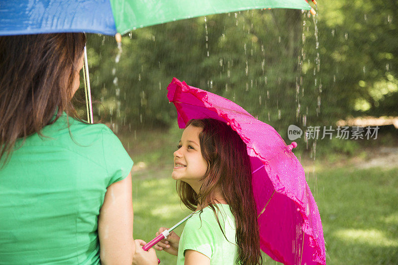 带着粉红色雨伞的孩子抬头望着雨中的妈妈。