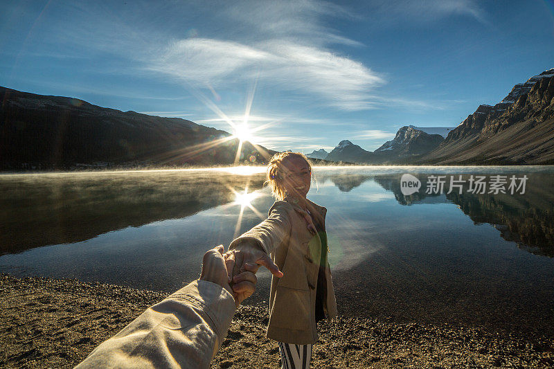 日出时分，一对年轻夫妇手牵着手沿着湖岸散步