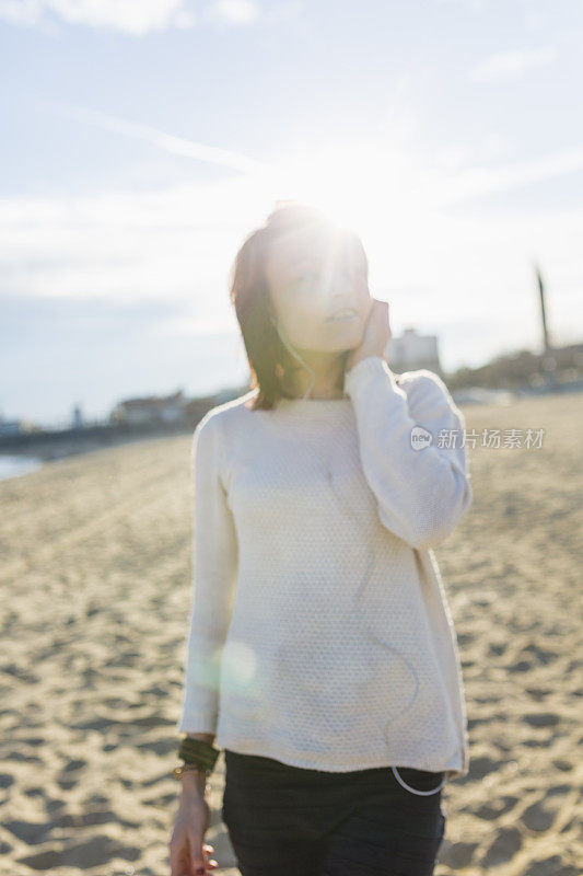 年轻女子在海滩上戴着耳机听音乐