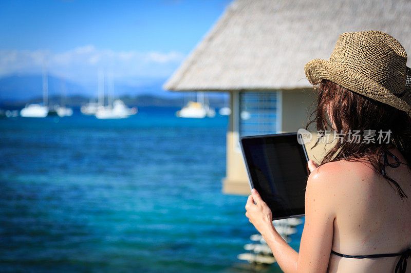 一名妇女在水上别墅阳台上使用电子平板电脑