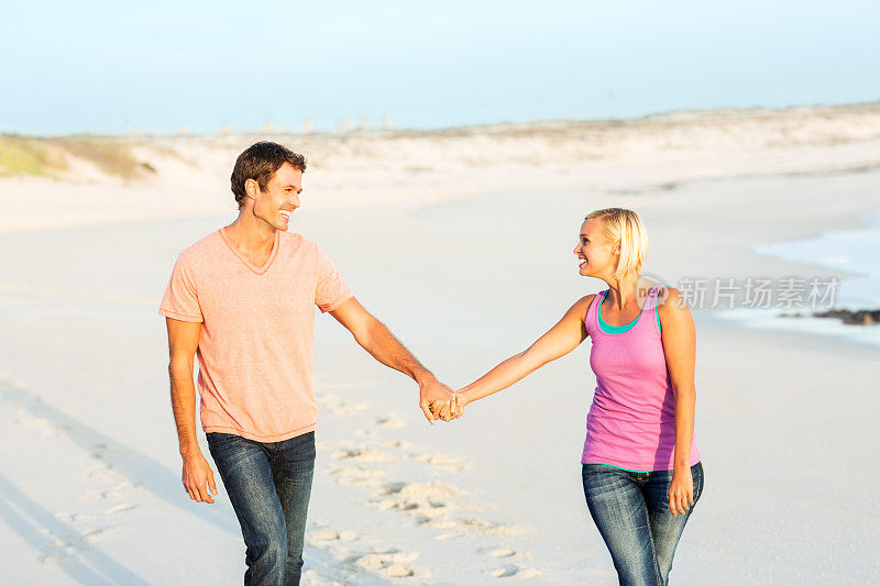 好玩的夫妇手牵着手在海滩上散步