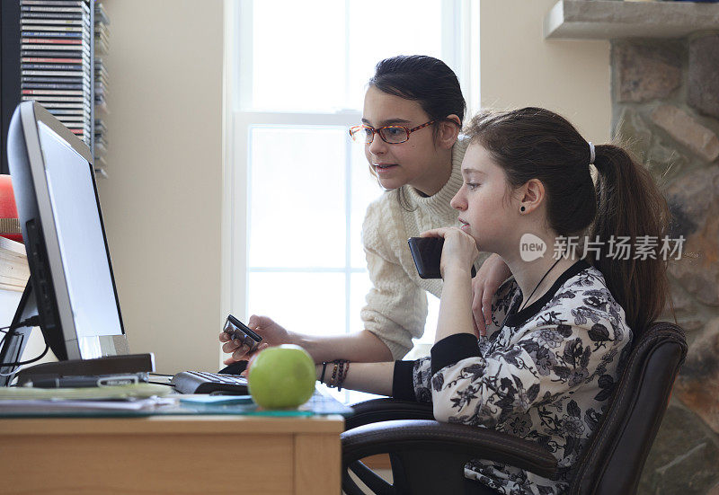 两个十几岁的女孩，姐妹，正在用台式电脑工作