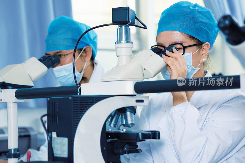 两个科学家在实验室里通过显微镜观察