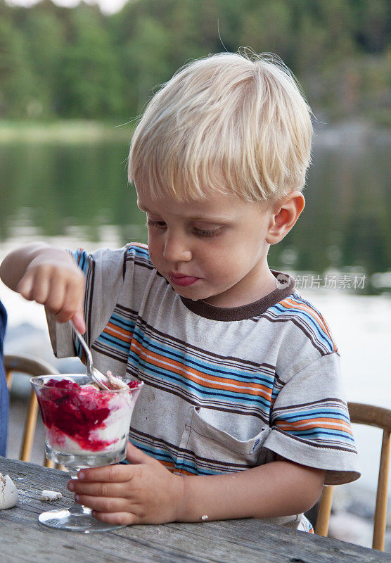 金发小男孩全神贯注地吃着甜点。在户外,斯德哥尔摩群岛。