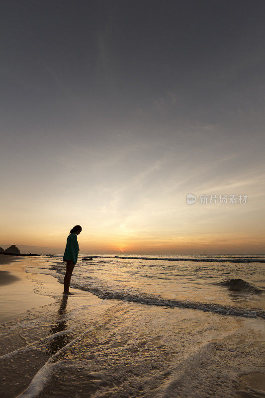在费尔南多迪诺罗尼亚荒芜的海滩上，女孩裹着沙滩浴巾凝视黄昏