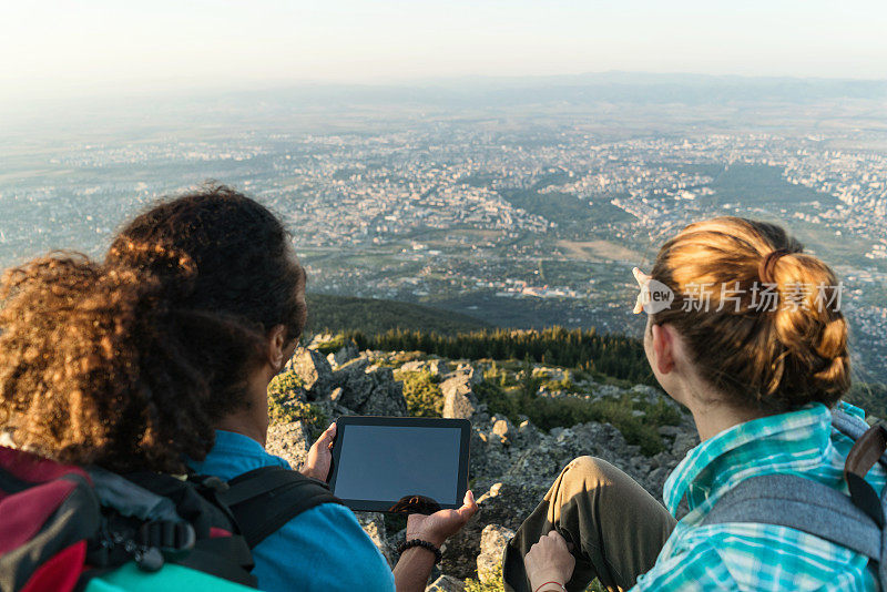 异族夫妇坐在山上的岩石上浏览平板电脑