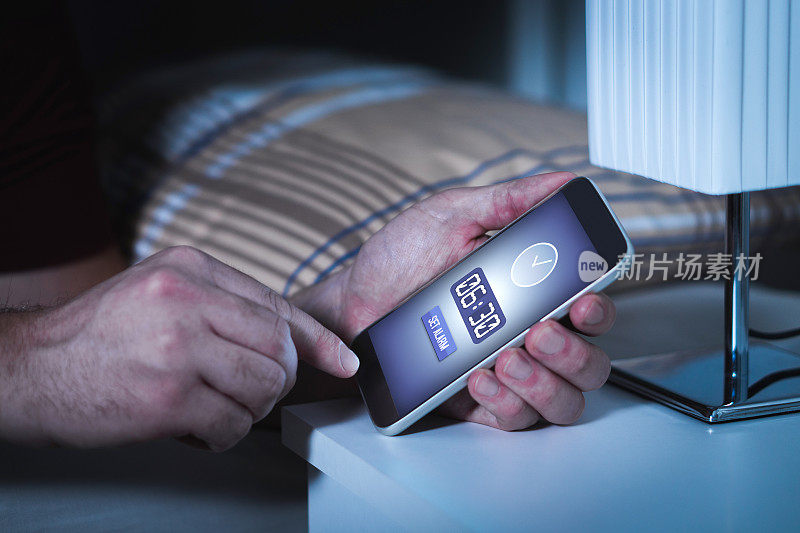 男子在晚上睡觉前用智能手机设定闹钟。手机里的时钟。