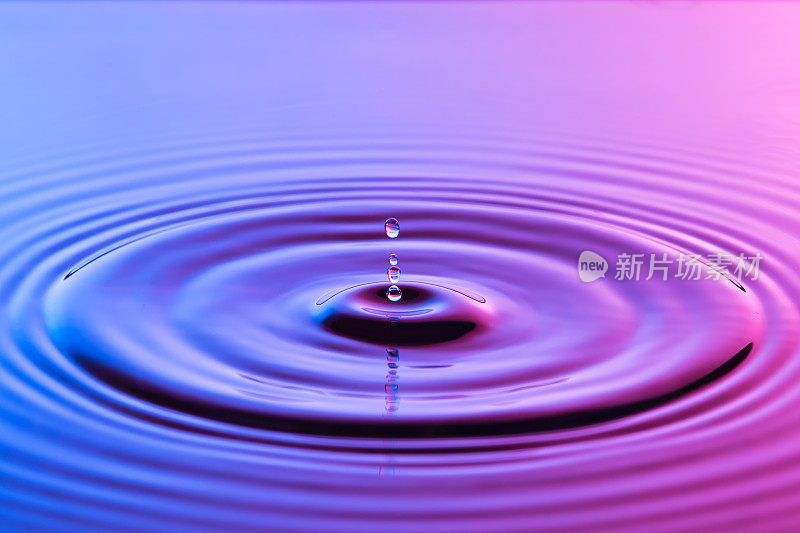 水滴近距离与同心涟漪在五颜六色的蓝色和粉红色的表面