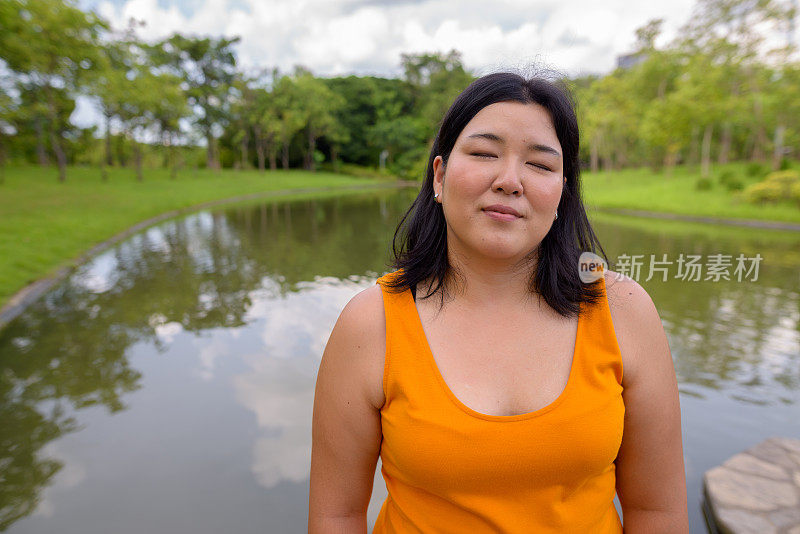 肖像超重的亚洲妇女穿着黄橙色的衣服放松在曼谷的公园在泰国