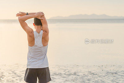 年轻的亚洲男子在海滩上奔跑，夕阳为背景