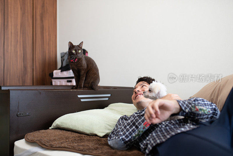 男人在床上抱着小狗，猫坐在床角上