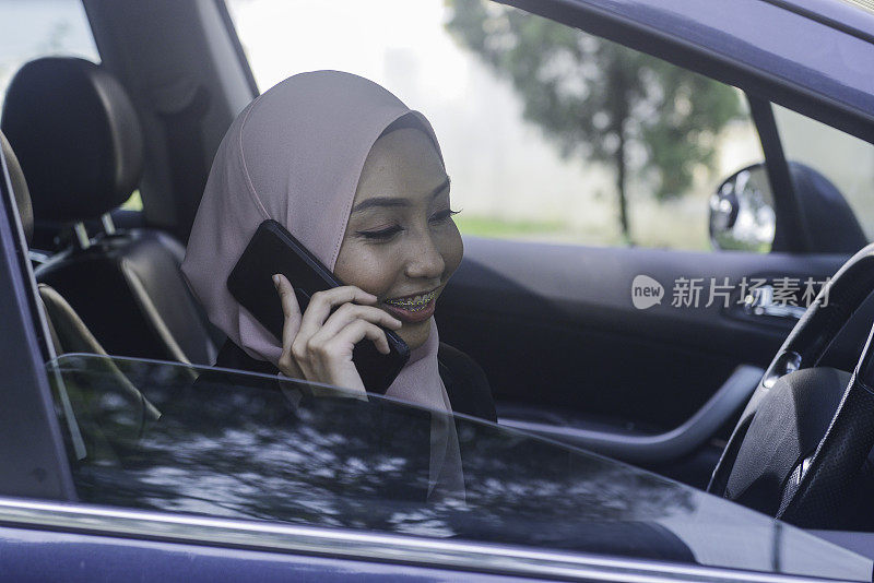 亚洲穆斯林女性司机在汽车中使用智能手机