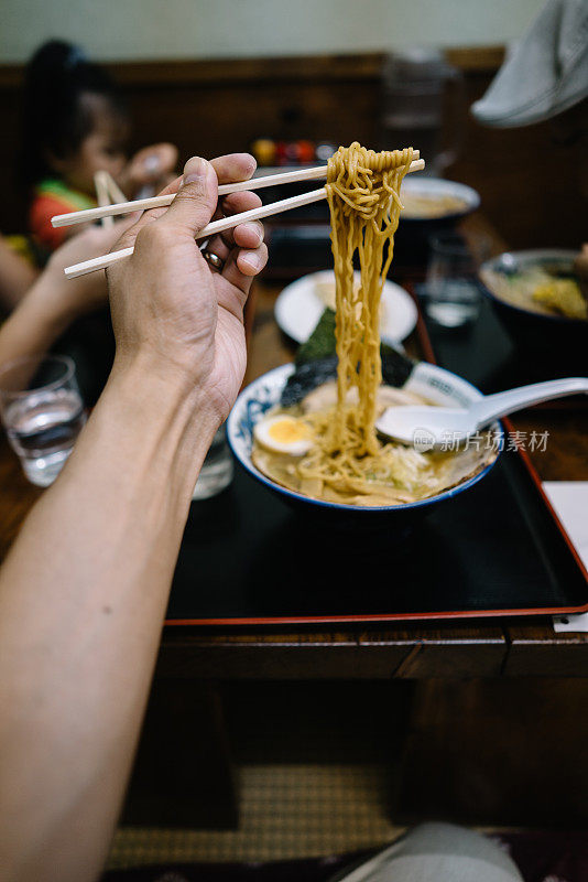 一个男人用筷子夹着面条在他面前