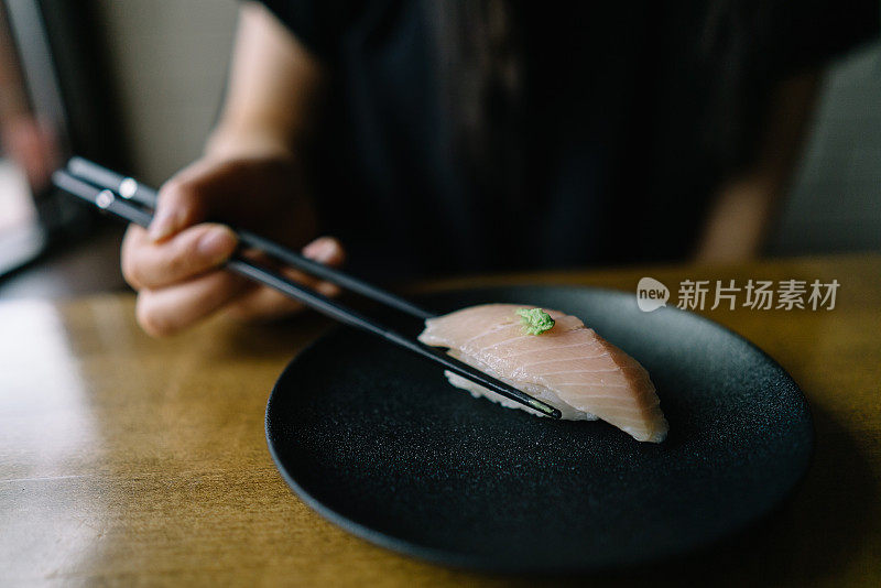 一个人正在用筷子夹起一片烤生鱼片寿司