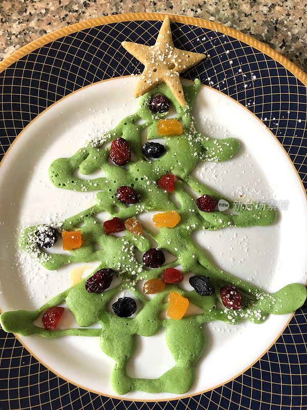 圣诞儿童早餐的绿色煎饼形状的圣诞树与糖霜糖的形象，圣诞树煎饼装饰饼干刀星星顶部，装饰物健康食用干果，如葡萄干，小葡萄干，蔓越莓，红醋栗，杏子