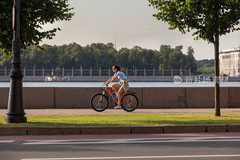 年轻的运动妇女在河边的城市堤岸上骑自行车