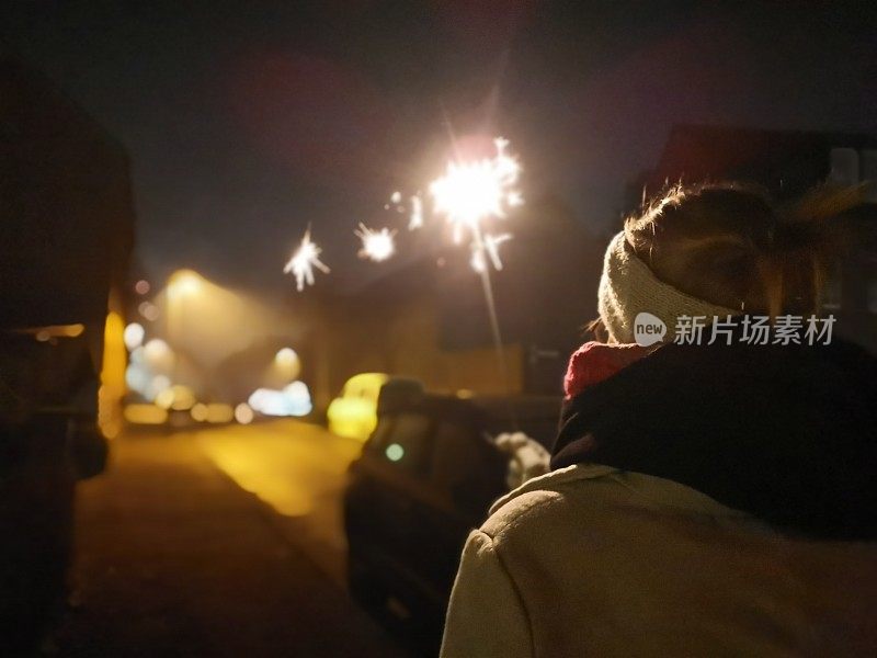 一名年轻女子观看新年前夜的庆祝活动，并手持自己的烟花参与其中