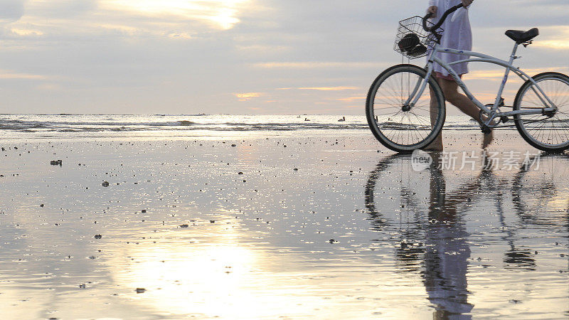 成熟的夫妇在日出时把自行车推下海滩