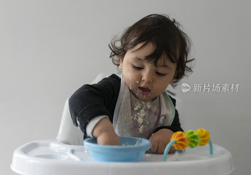 可爱的小男孩在一团乱麻中学习自食其力，坐在高高的椅子上