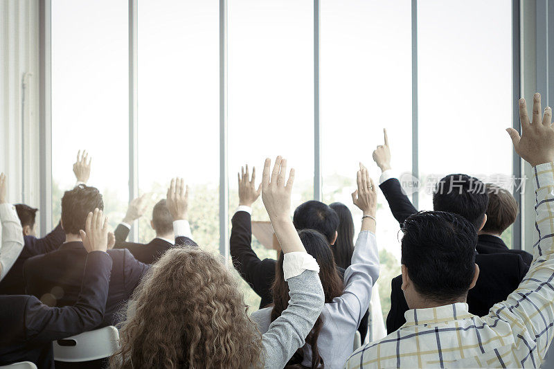 商务人士在会议中与演讲者举手提问，在会议中举手同意或投票表决意见