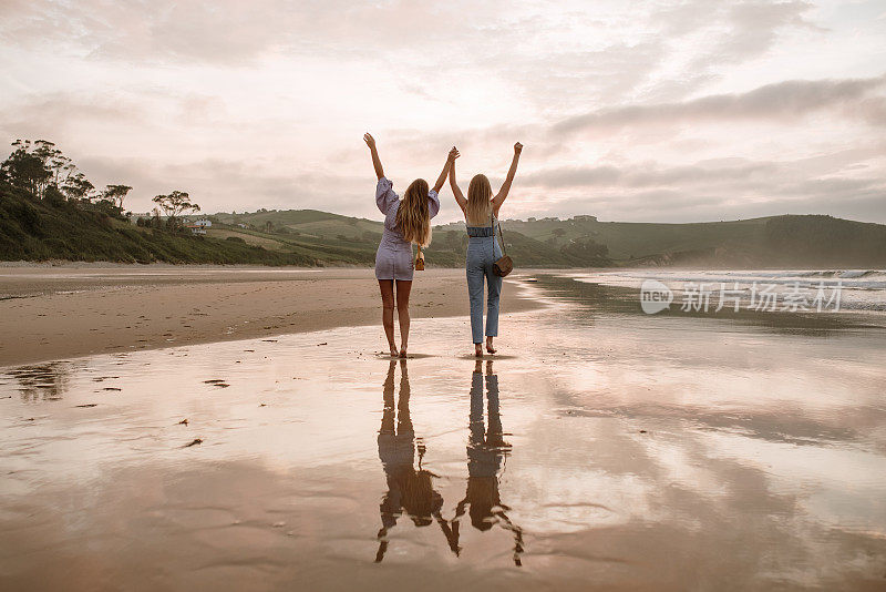 两名年轻女子在海滩上举起手臂的后视图