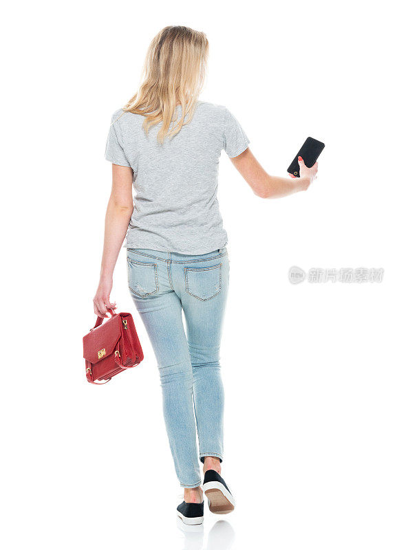 白人女性走在白色背景，穿着裤子，拿着公文包，使用手机