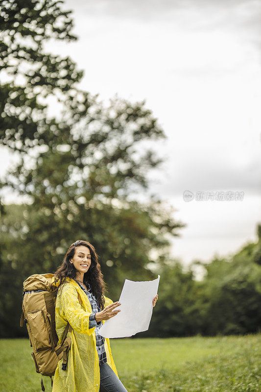 年轻女子穿着防水夹克，看地图，在雨中徒步旅行