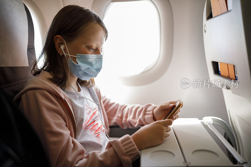可爱的小女孩戴着面罩在飞机上使用手机