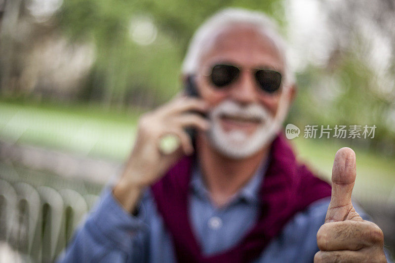 老人愉快地讲电话，笑出声来——一个老人正在户外讲手机