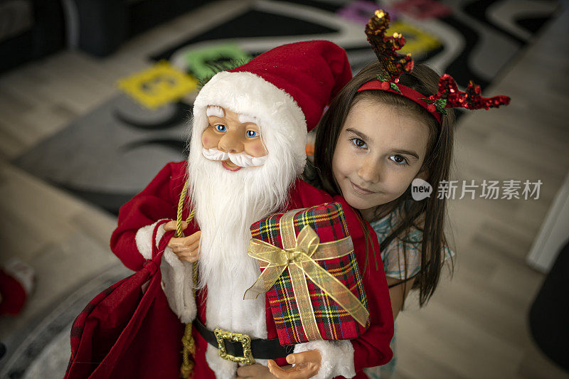 一个漂亮的女孩抱着一个大圣诞老人玩具