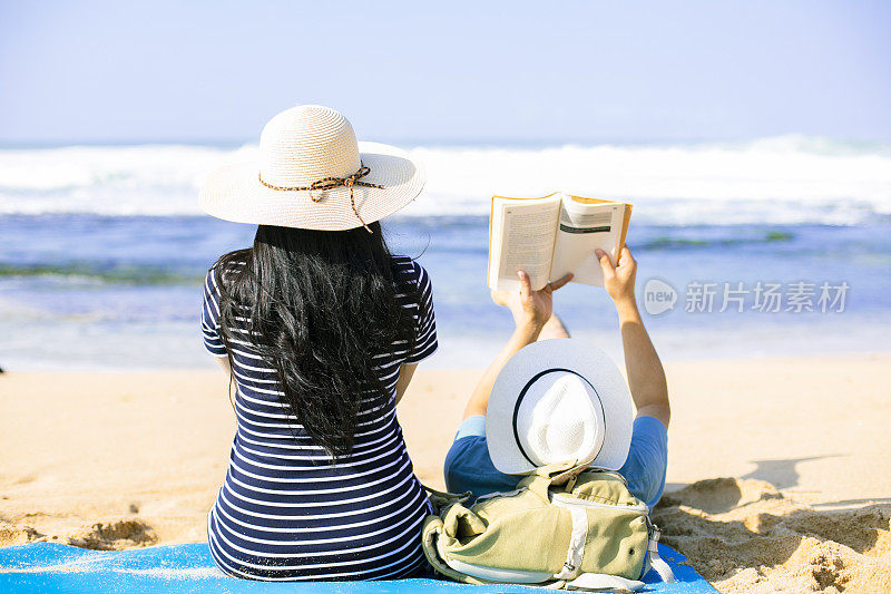 一对亚洲年轻夫妇坐在海滩上遥望远方