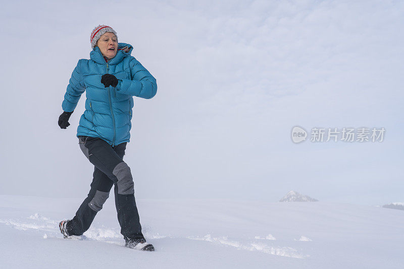 成熟的女人穿着皮大衣在雪地里奔跑