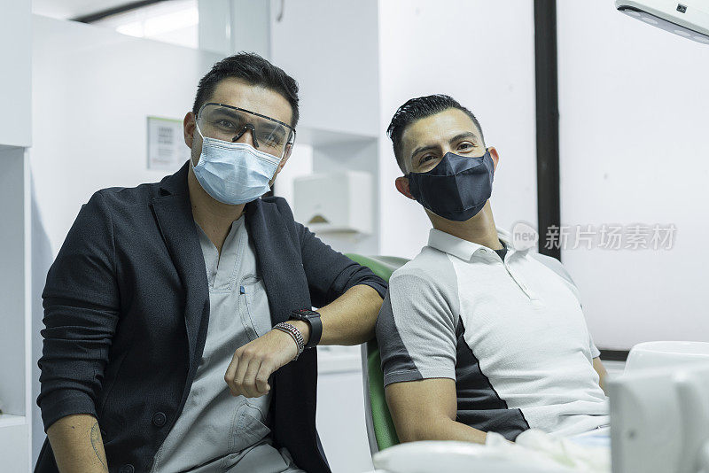 一名拉丁裔医生和他的病人坐在牙科诊所看着摄像机的肖像