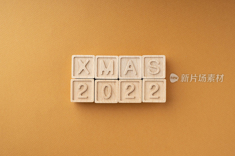 木块上写着2022年圣诞节。橙色背景上有字母和数字的木制立方体。新年卡