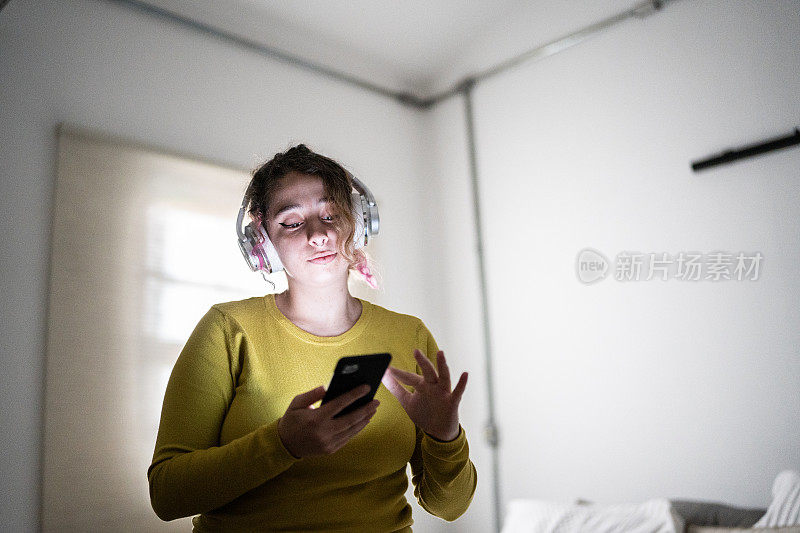 年轻女子在家戴着耳机用手机听音乐