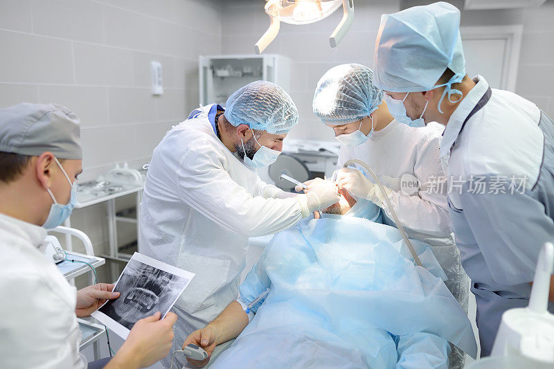 牙科手术中的外科医生和护士。进行外科牙科手术的医疗队。手术室里被麻醉的病人。在诊所安装种植牙。