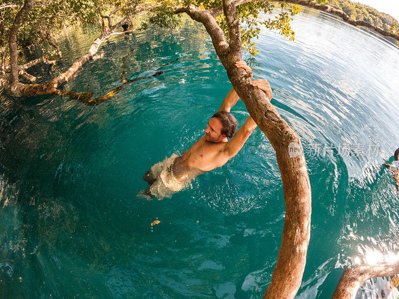 一个人挂在热带天然井的树上，尽情享受大自然