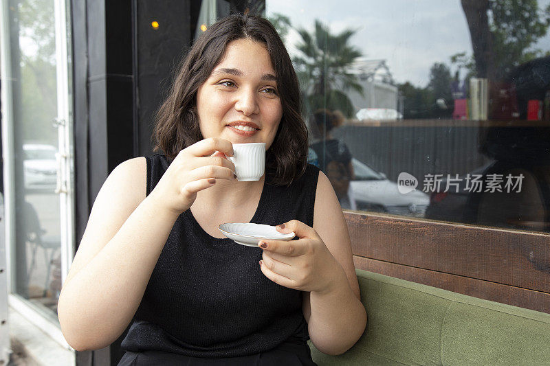年轻美丽快乐的女人享受咖啡在街头咖啡馆