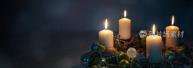 夜晚的灯光，四个白色的降临节蜡烛在花环上与圣诞装饰在深蓝色的背景下，全景格式，复制空间，选择焦点