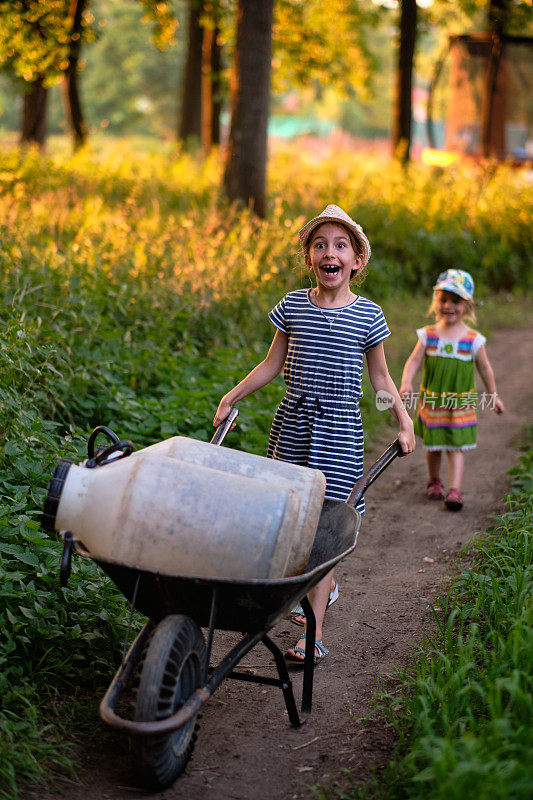 在一个公共有机花园里，一个小女孩用手推车搬运木桶，去收集河水灌溉他们的田地
