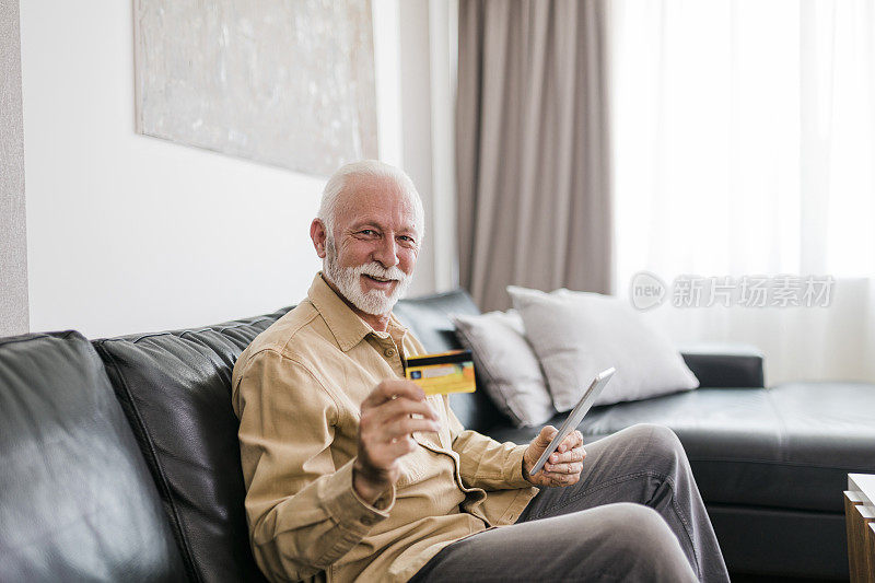 一个年长的成年男子用他的卡片和电子平板电脑在家里网上购物的镜头